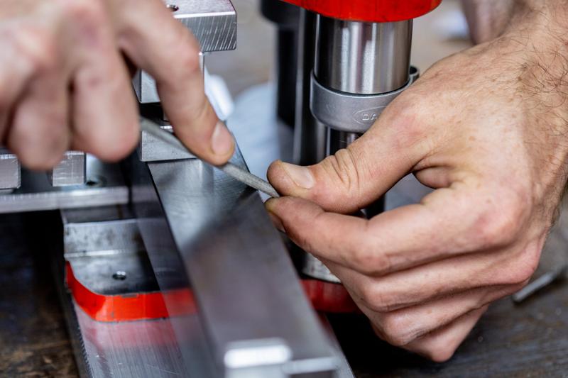 Hands finishing a component on a red jig at DW Plastics