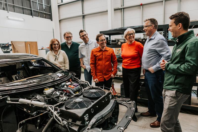 A group viewing a stripped vehicle in a workshop