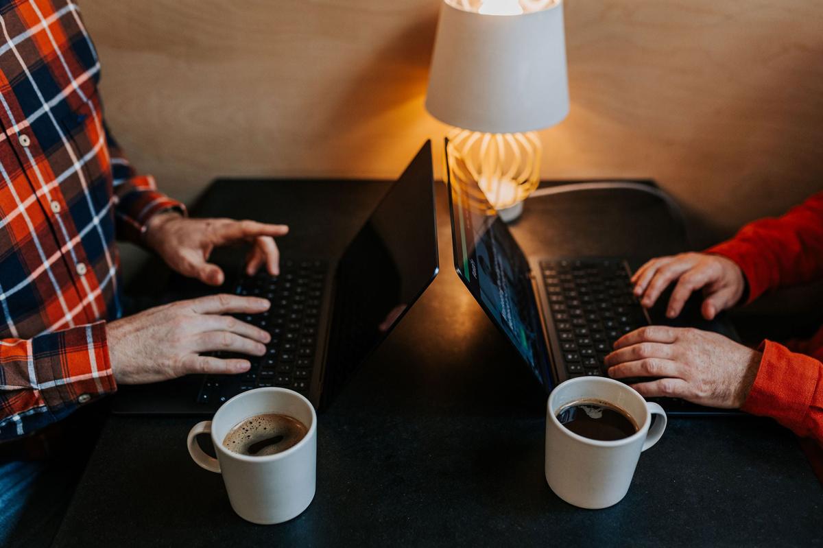 Close-up of marketing team members typing on laptops with cups of coffee