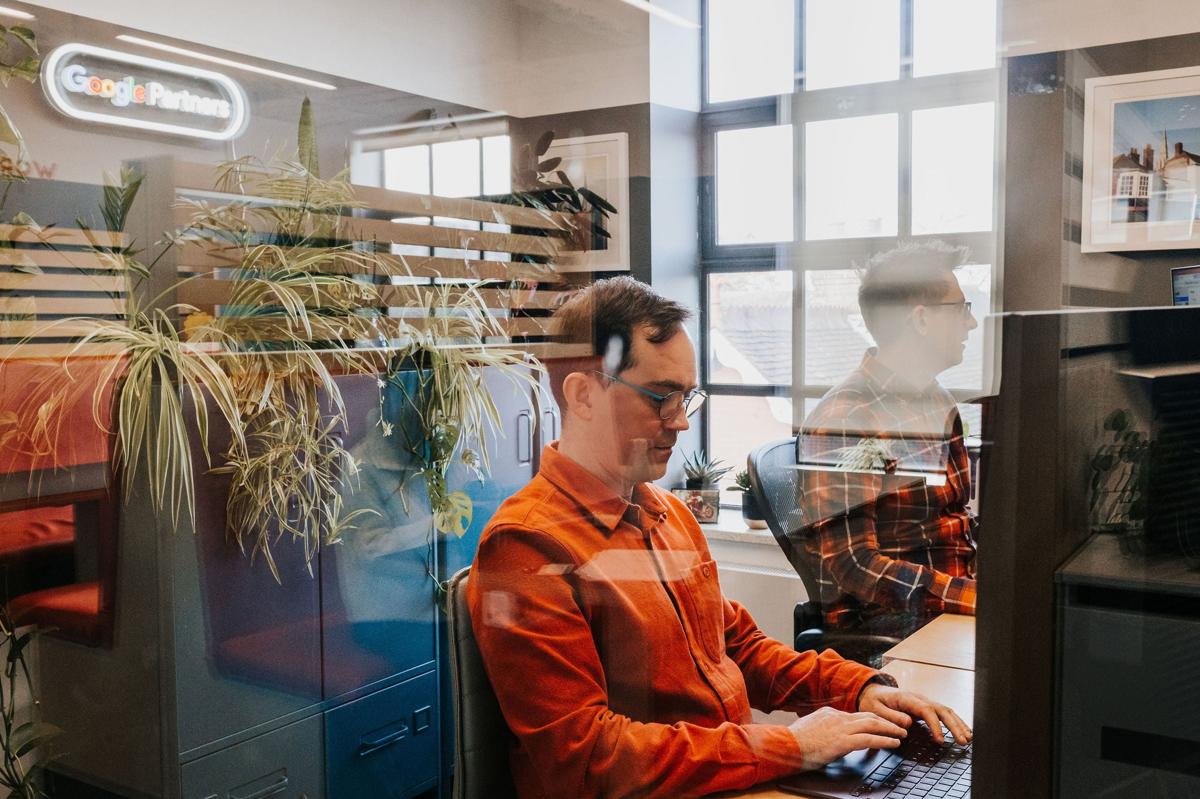 A Pallant marketer working at a studio desk beside a plant