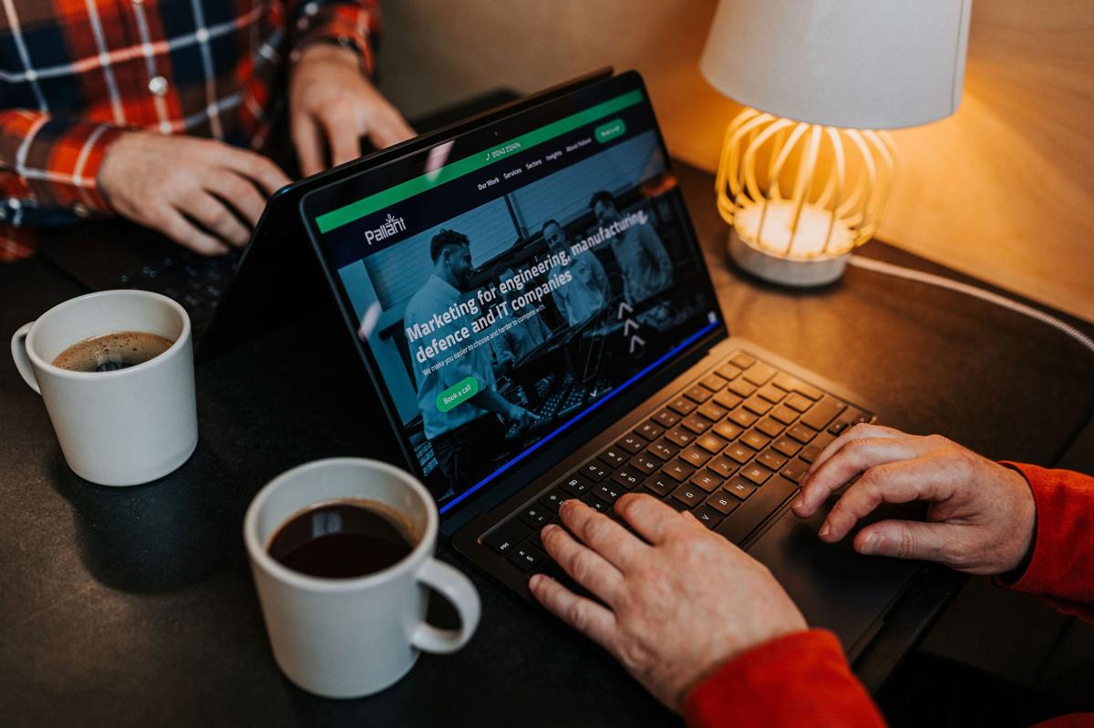 Hands working on a marketing website on a laptop beside a coffee